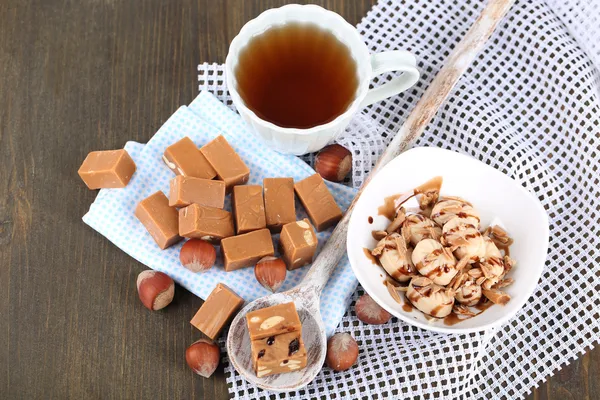 Many toffee in spoon and cup of tea on napkins on wooden table
