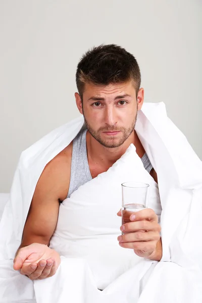 Handsome young man with sleeping pills on gray wall background