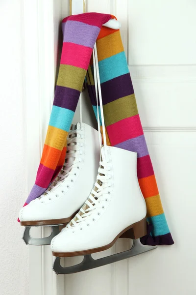 Figure skates hanging on a door knob with scarf