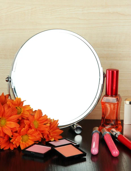 Round table mirror with cosmetics and flowers on table on wooden background