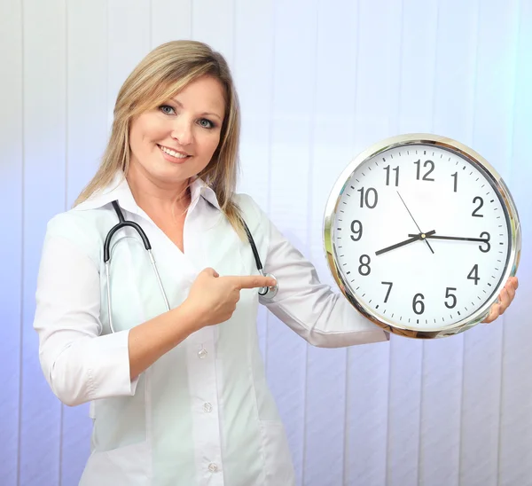 Young beautiful doctor with stethoscope and clock, on light background