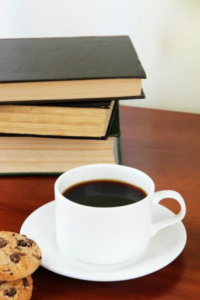 Cup of coffee with cookies and books on wooden table on bright background