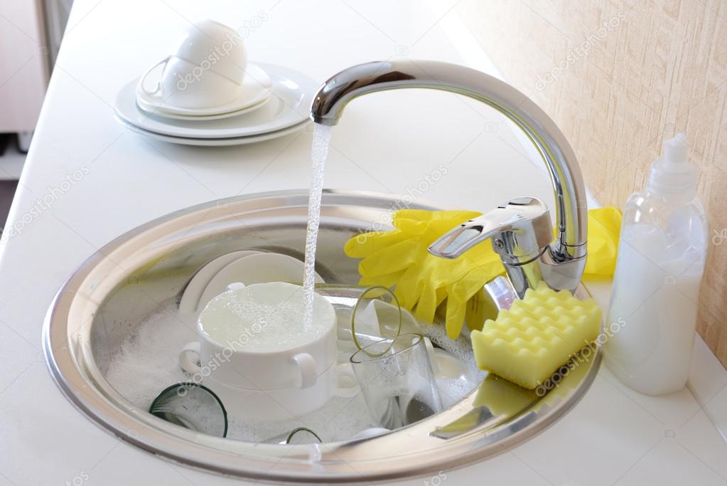 Stack of dishes soaking in kitchen sink — Stock Photo © belchonock 35023741