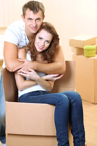 Young couple with boxes in new home on room background