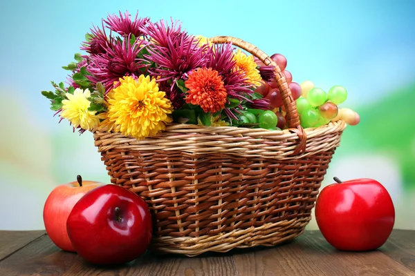 Composition with beautiful flowers in wicker basket and fruits, on bright background