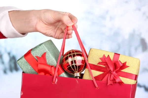 Hand holds package with New Year balls and gifts on snow background