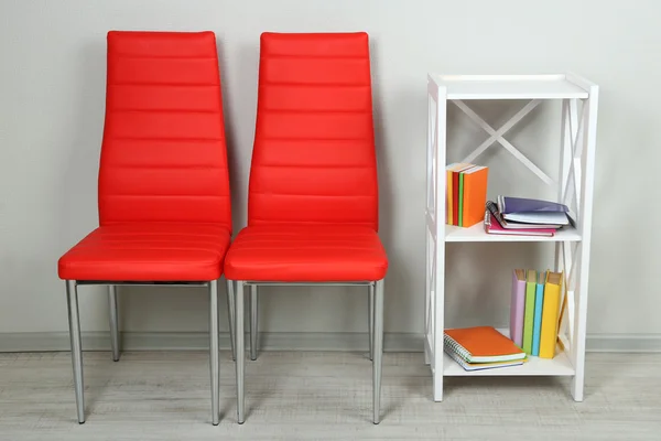 Beautiful interior with modern color chairs, books on wooden stand, on wall background