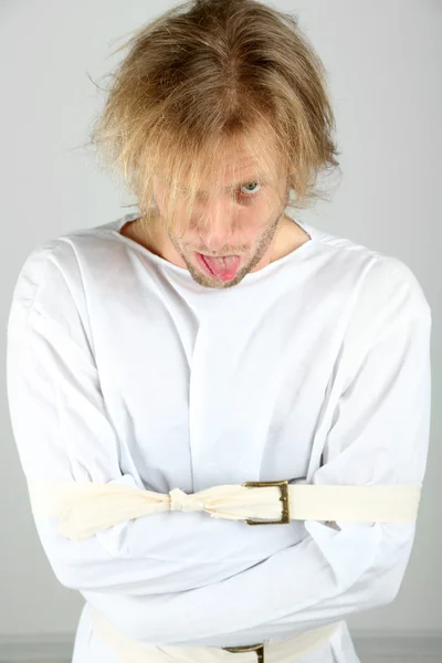 Mentally ill man in strait-jacket on gray background