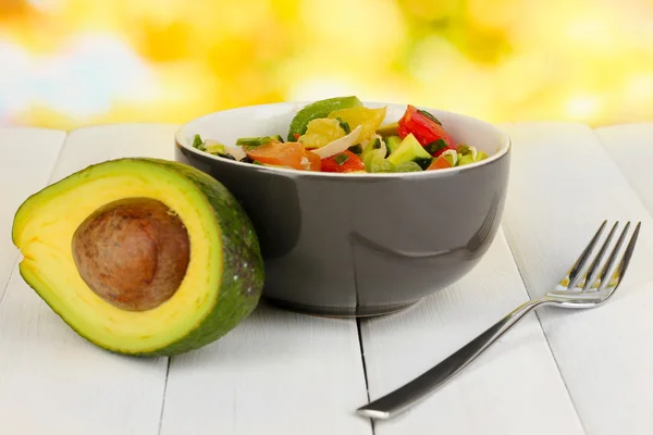Tasty avocado salad in bowl on wooden table on natural background