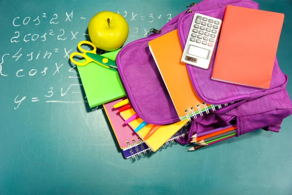Purple backpack with school supplies on green desk background