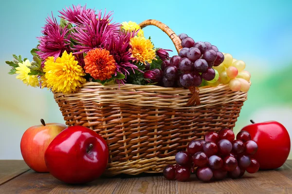 Composition with beautiful flowers in wicker basket and fruits, on bright background