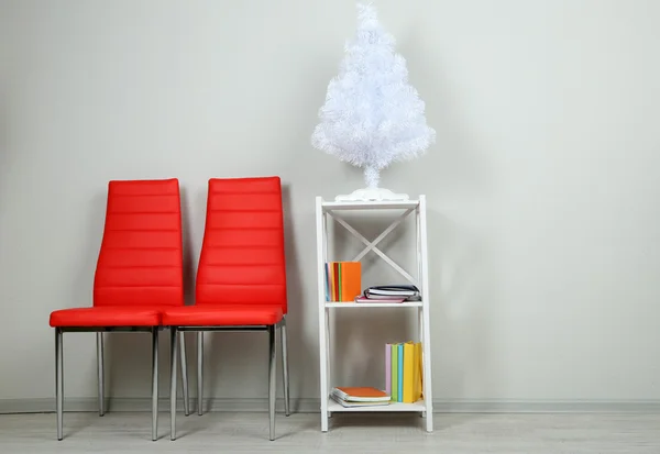 Beautiful interior with modern color chairs, books on wooden stand, on wall background