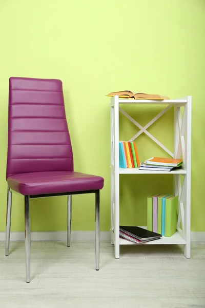 Beautiful interior with modern color chair, books on wooden stand, on wall background