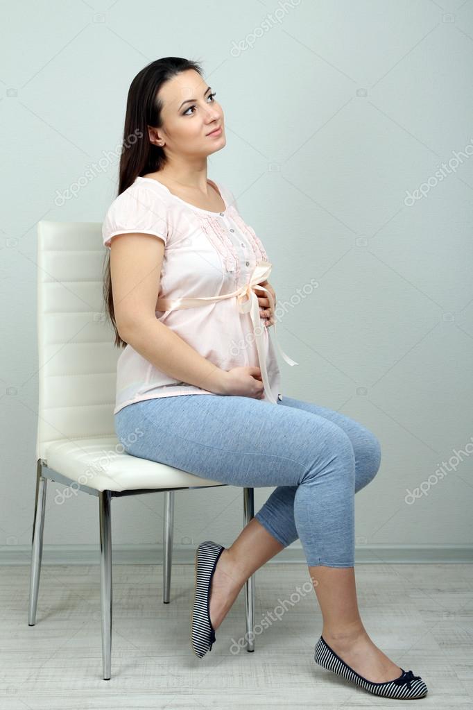 Young pregnant woman sitting on chair on wall background — Stock 