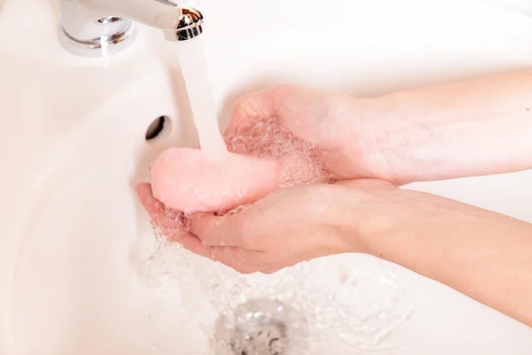 Close-up of human hands being washed under faucet in bathroom