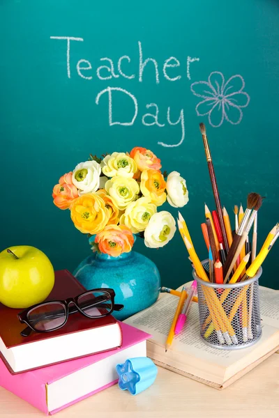 School supplies and flowers on blackboard background with inscription Teacher Day