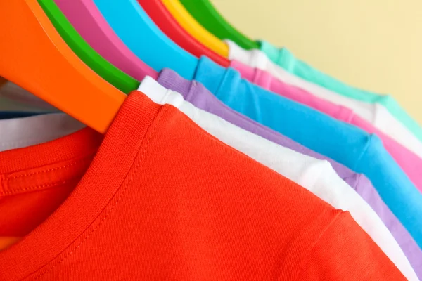 Different shirts on colorful hangers on beige background