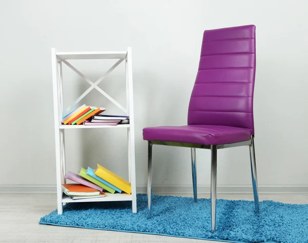 Beautiful interior with modern color chair, books on wooden stand, on wall background