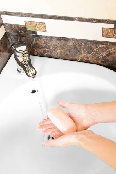 Close-up of human hands being washed under faucet in bathroom