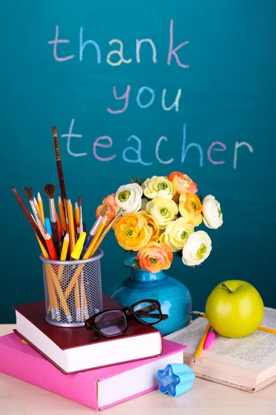 School supplies and flowers on blackboard background with inscription Thank you teacher
