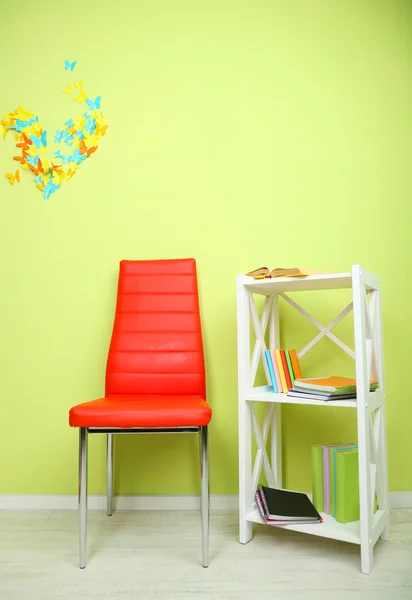 Beautiful interior with modern color chair, books on wooden stand, on wall background