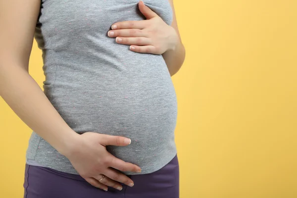 Pregnant woman touching her belly on yellow background
