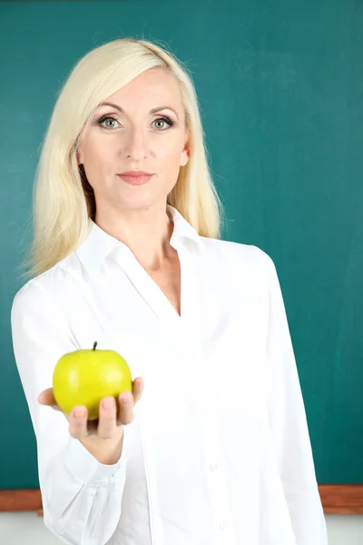 School teacher near blackboard with apple in classroom