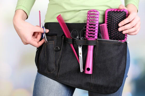 Woman hairdresser with tool belt on bright background