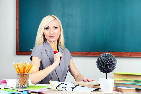 School teacher sitting at table on blackboard background