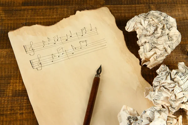 Crumpled paper balls with ink pen and music sheet on wooden background