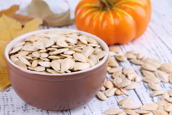 Pumpkin seeds in bowl with pumpkin on wooden background