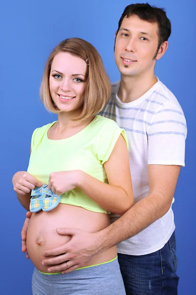 Pregnant woman holding baby shoes with her husband on blue background