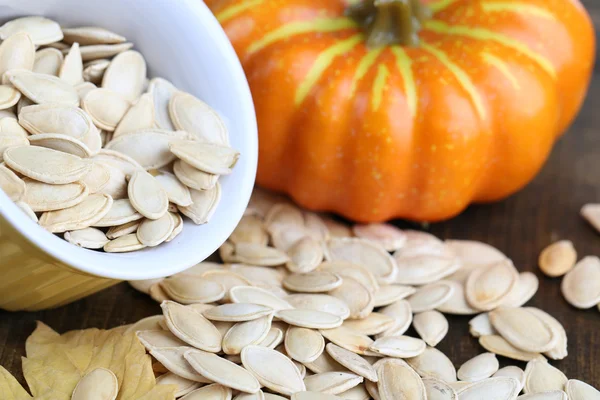 Pumpkin seeds in bowl with pumpkin on table close up