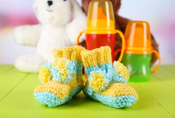 Composition with crocheted booties for baby, bottle, toy and other things on color background