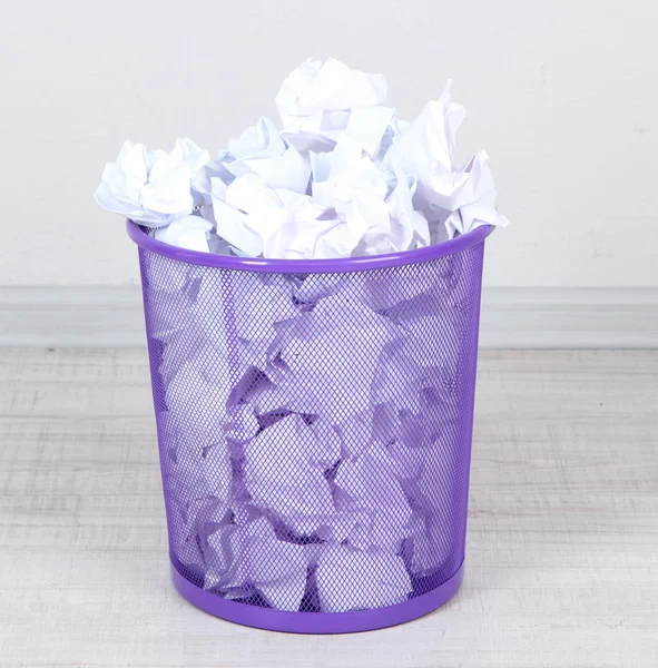 Recycle bin filled with crumpled papers, on floor