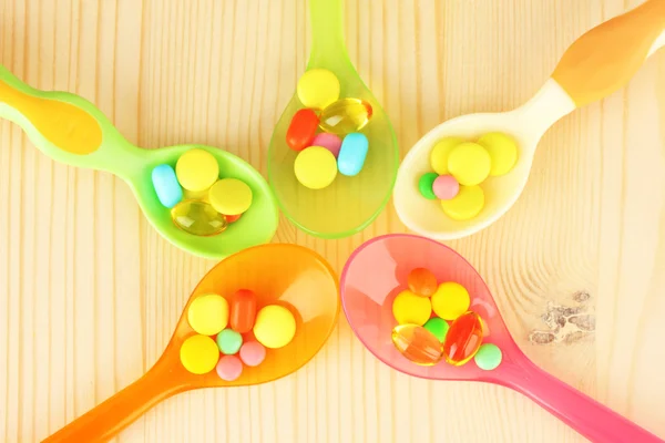 Plastic spoons with color pills on wooden background