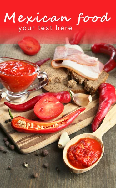Composition with salsa sauce on bread, red hot chili peppers and garlic, on sackcloth, on wooden background