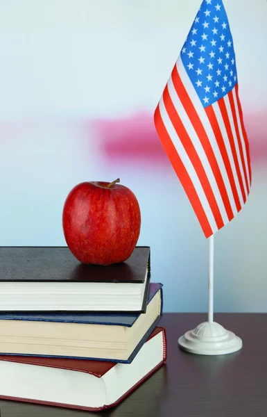 Composition of American flag, books and apple on wooden table, on light background