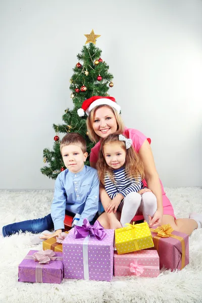 Nice mother and her children with gifts near decorating Christmas tree in room