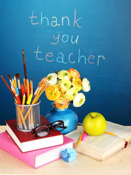 School supplies and flowers on blackboard background with inscription Thank you teacher