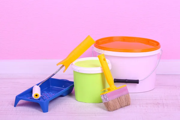 Paints, roll and paintbrush on floor in room on wall background