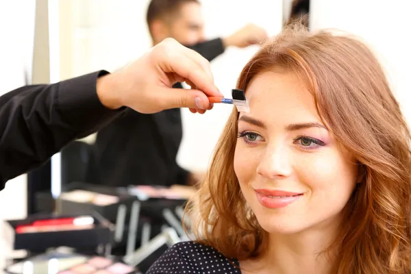 Young guy stylist doing makeup beautiful woman in beauty salon