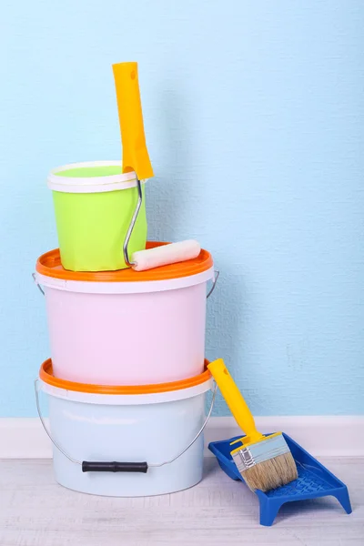 Paints, roll and paintbrush on floor in room on wall background