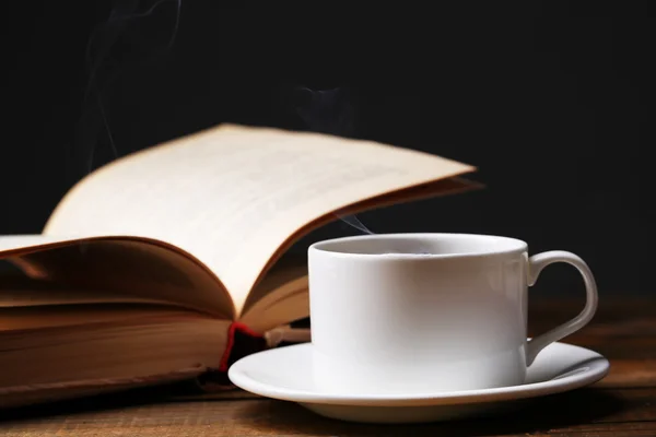 Cup of hot coffee with book on table on dark background