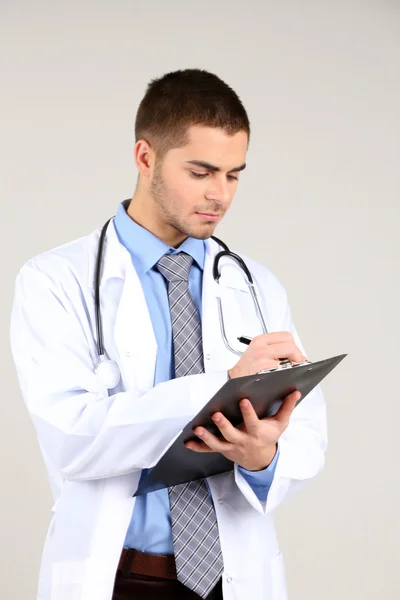 Male Doctor standing with folder, on gray background