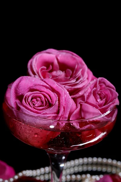 Composition with pink sparkle wine and roses in glass, isolated on black