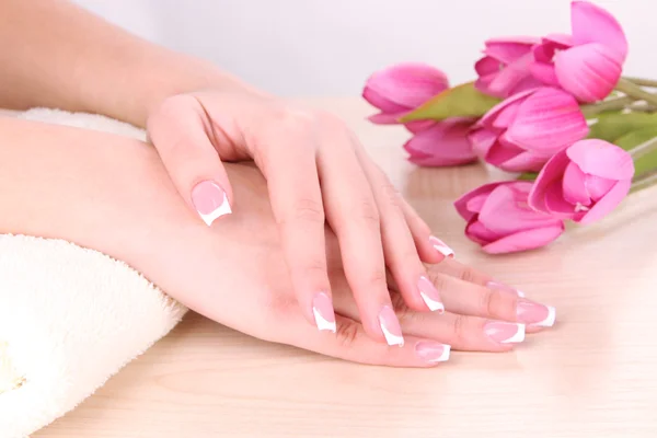 Beautiful woman hands with french manicure and flowers on table on white background