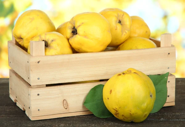 Sweet quinces in wooden box on table on bright background