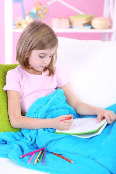 Little girl draws sitting on sofa in room