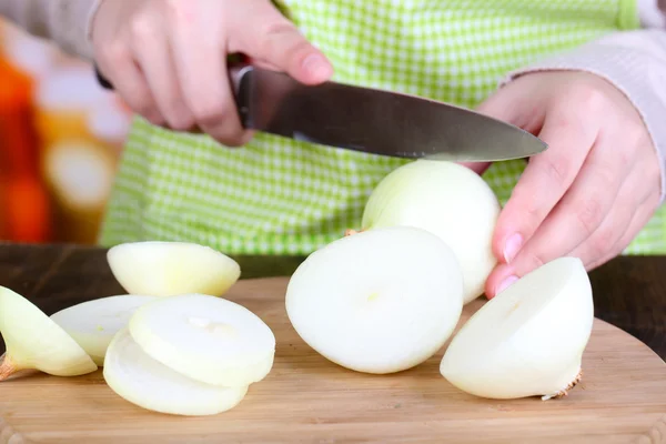 Female hands cutting bulb onion, on kitchen background